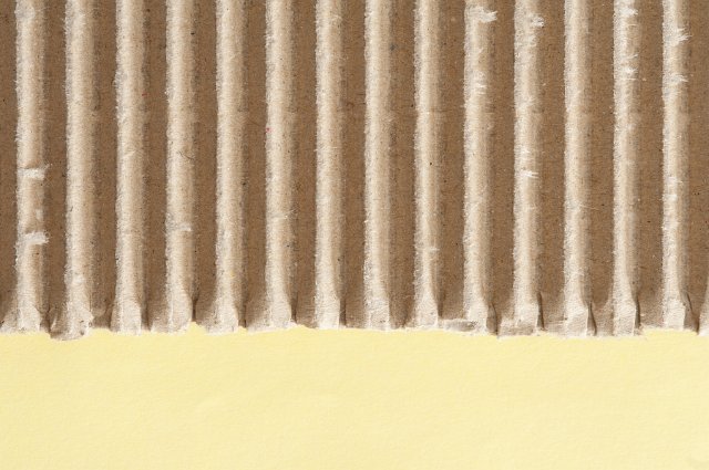 Corrugated brown cardboard texture with yellow copy space below in a close up detailed view from above of paper packaging