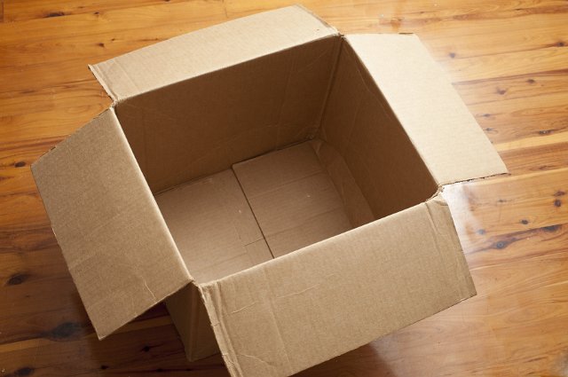 High Angle View of Empty Cardboard Box with Open Flaps on Shiny Hardwood Floor - Moving or Shipping Concept Image