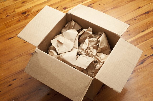 Open brown cardboard packing box with crumpled brown paper for packaging inside on a wooden floor, high angle view