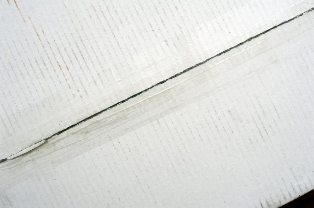 Packaging tape on a white carton sealing the two flaps for transport, close up view from above